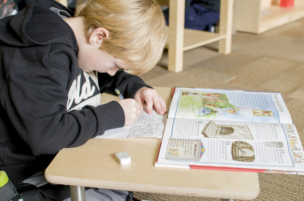 A toddler with short blond hair focusing on a project